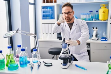 Fototapeta premium Middle age caucasian man working at scientist laboratory pointing with finger to the camera and to you, confident gesture looking serious