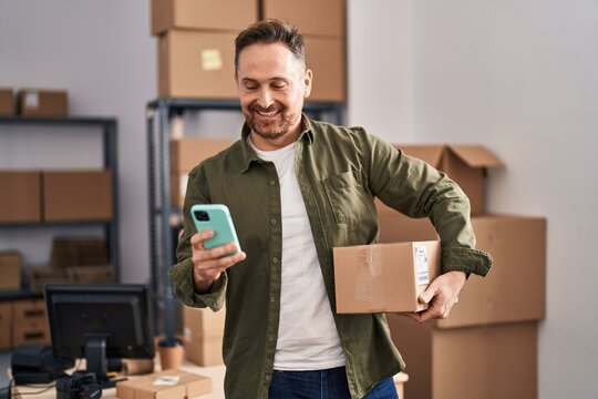 Young caucasian man ecommerce business worker using smartphone holding package at office