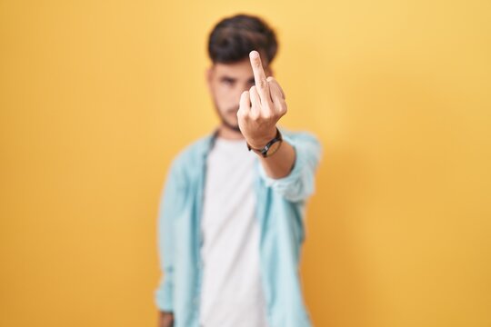 Young Hispanic Man With Tattoos Standing Over Yellow Background Showing Middle Finger, Impolite And Rude Fuck Off Expression