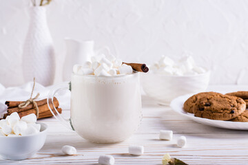 Warm cocoa with marshmallows and cinnamon in a cup and a plate of oatmeal cookies on the table.