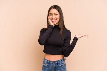 Young colombian woman isolated on beige background holds copy space on a palm, keep hand over...