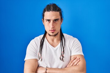 Hispanic man with long hair standing over blue background skeptic and nervous, disapproving expression on face with crossed arms. negative person.