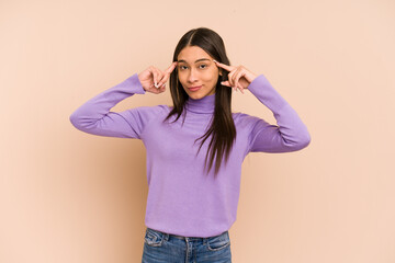 Young colombian woman isolated on beige background focused on a task, keeping forefingers pointing head.