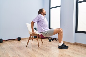 Middle age man smiling confident sitting on chair stretching at sport center