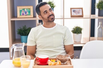 Fototapeta na wymiar Hispanic man with beard eating breakfast looking to side, relax profile pose with natural face and confident smile.