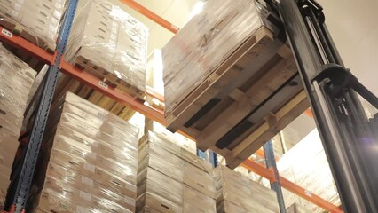 Forklift lifts a pallet of boxes onto a rack in a logistics warehouse