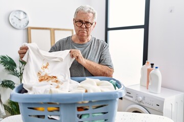 Senior caucasian man holding dirty t shirt with stain relaxed with serious expression on face. simple and natural looking at the camera.
