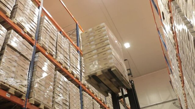 Loading and unloading goods in a logistics warehouse using a forklift. Boxes on a pallet are lifted onto racks