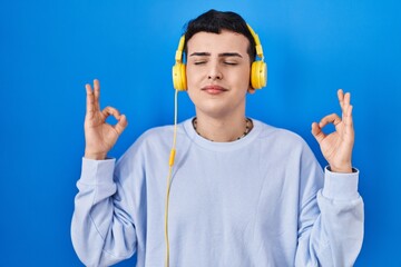 Non binary person listening to music using headphones relaxed and smiling with eyes closed doing meditation gesture with fingers. yoga concept.