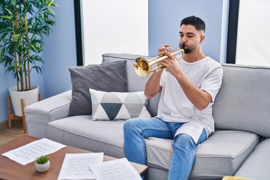 Young Arab Man Musician Playing Trumpet Sitting On Sofa At Home