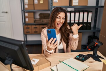 Young brunette woman working at small business ecommerce doing video call pointing thumb up to the side smiling happy with open mouth