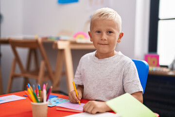Adorable toddler student drawing on notebook sitting on table at classroom