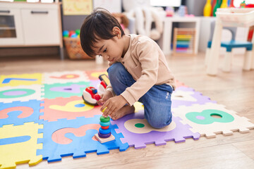 Adorable hispanic boy playing with hoops toys sitting on floor at kindergarten © Krakenimages.com