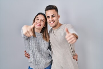 Young hispanic couple standing over white background approving doing positive gesture with hand,...