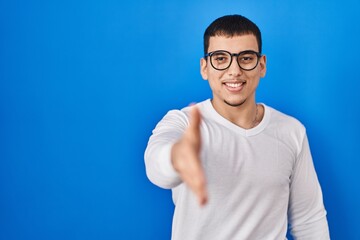Young arab man wearing casual white shirt and glasses smiling friendly offering handshake as greeting and welcoming. successful business.