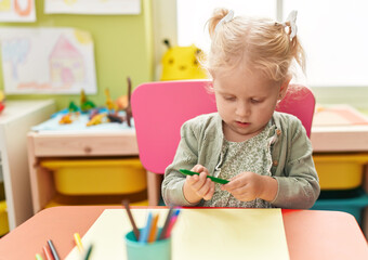 Adorable blonde girl preschool student sitting on table drawing on paper at kindergarten