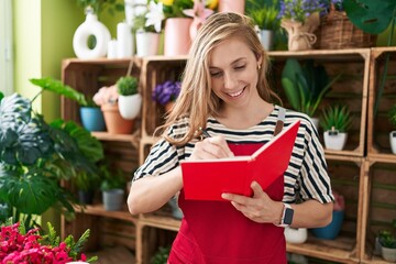 Young blonde woman florist smiling confident writing on notebook at flower shop