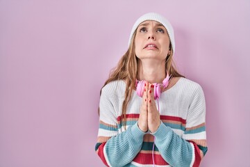 Young blonde woman standing over pink background begging and praying with hands together with hope...