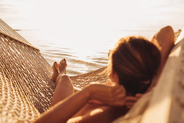 Young woman relaxing in wicker hammock on the sandy beach on Mauritius coast and enjoying sunset...