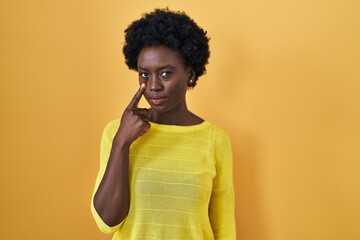Fototapeta na wymiar African young woman standing over yellow studio pointing to the eye watching you gesture, suspicious expression