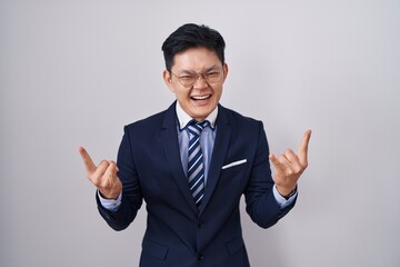 Young asian man wearing business suit and tie shouting with crazy expression doing rock symbol with hands up. music star. heavy music concept.