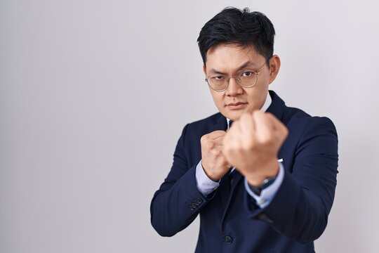 Young asian man wearing business suit and tie ready to fight with fist defense gesture, angry and upset face, afraid of problem