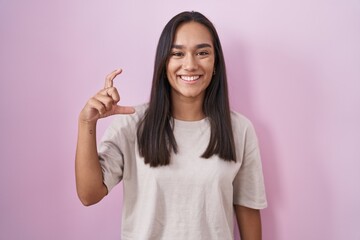 Young hispanic woman standing over pink background smiling and confident gesturing with hand doing...