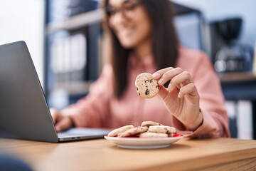 Young hispanic woman business worker using laptop eating cookies at office
