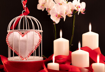 Composition pour la Saint-Valentin avec un cœur blanc et rouge dans une cage à oiseau et des bougies.
