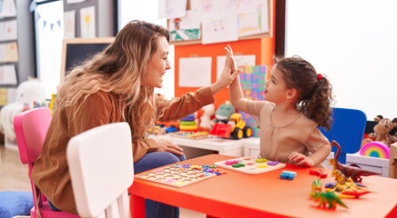 Fototapeta Adorable hispanic girl playing with maths puzzle game high five with teacher at kindergarten obraz