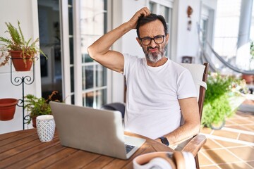 Middle age man using computer laptop at home confuse and wondering about question. uncertain with...