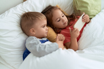 Obraz na płótnie Canvas Adorable girl and boy watching video on smartphone lying on bed at bedroom
