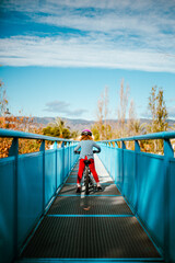Niña en bici sobre un puente en el parque. Cielo bonito y ropa colorida.