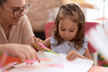 Teacher and toddler smiling confident cutting paper at kindergarten