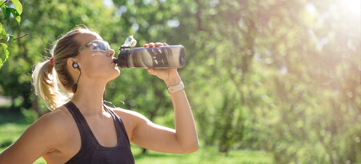 Middle-aged slim caucasian woman sportswear drink water from sport bottle while running, jogging training in park in sunny day summer. Leisure activity, healthy lifestyle. Banner copy space