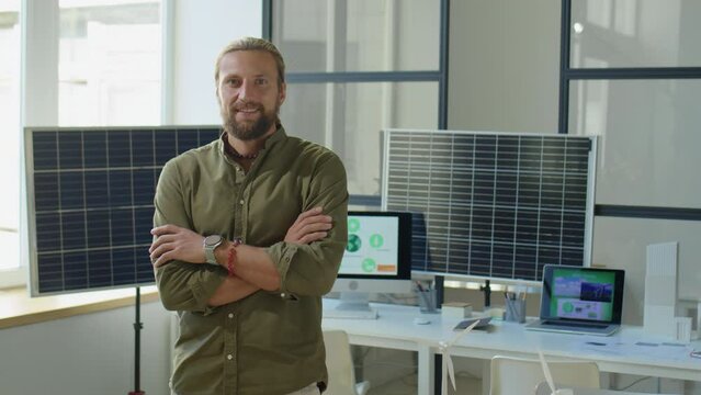 Medium shot of male renewable energy developers smiling and posing for camera with arms crossed during workday in office with solar panels