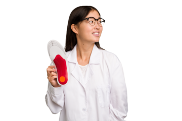 Young asian chiropodist holding a insoles for shoes isolated looks aside smiling, cheerful and pleasant.
