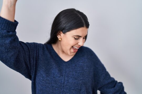 Young brunette woman standing over isolated background dancing happy and cheerful, smiling moving casual and confident listening to music