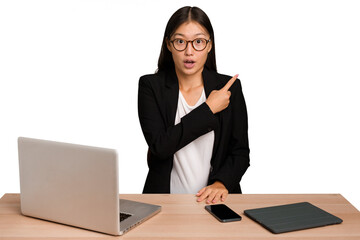 Young business asian woman sitting on a table isolated pointing to the side