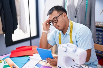 Young chinese man tailor using touchpad with serious expression at tailor shop