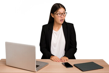 Young business asian woman sitting on a table isolated being shocked because of something she has seen.