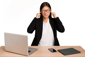 Young business asian woman sitting on a table isolated covering ears with fingers, stressed and desperate by a loudly ambient.