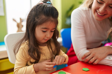 Teacher and toddler playing with maths puzzle game sitting on table at kindergarten