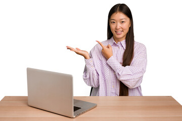 Young student asian woman in a workplace with a laptop isolated excited holding a copy space on...