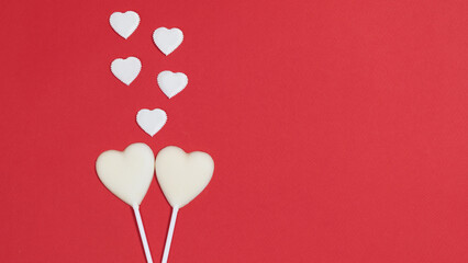 Two white heart shaped chocolates in love. A group of small hearts of symbols of love. Red background. Greeting card.