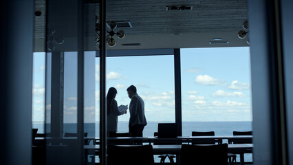 Business team silhouettes discussing ideas at beautiful sea view window. 