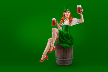 Happy Irish girl holding big mugs with beer or ale sitting on a barrel. Young red-haired woman аs...