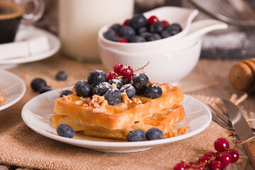 Waffles with red currant and blueberries on white dish.
