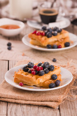 Waffles with red currant and blueberries on white dish.