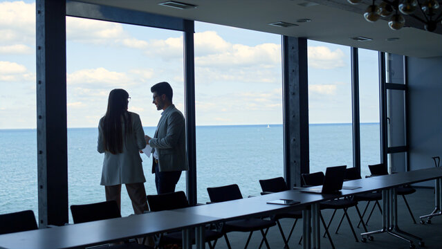 Business team discussing ideas at beautiful sea view window. Two managers work
